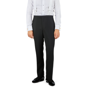 A person wearing **Baltzar Sartorial Black Wool Mohair Tuxedo Flat Front Trousers**, black shoes, a white dress shirt with gold cufflinks, and suspenders. Only the lower torso and legs are visible, presenting a sleek formal look.