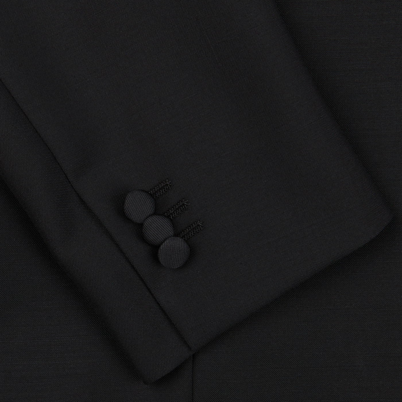 Close-up of the cuff of an eveningwear Black Wool Mohair Tuxedo Jacket sleeve by Baltzar Sartorial with three black buttons arranged vertically.