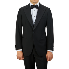 A man in a sleek Baltzar Sartorial Black Wool Mohair Tuxedo Jacket with a white dress shirt and a black bow tie stands against a plain background. His face is not shown, highlighting the sophistication of his eveningwear ensemble.