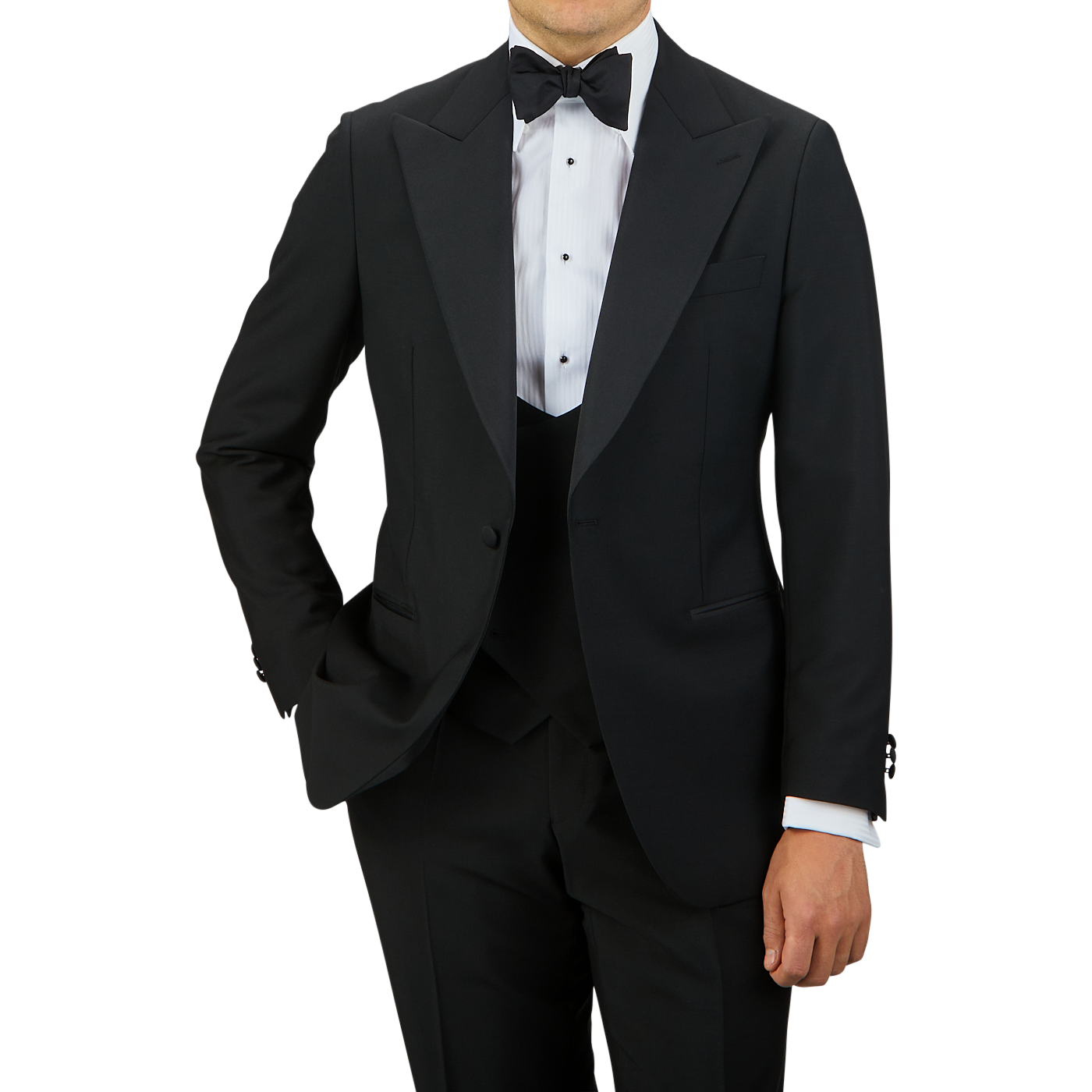 A person in a Black Wool Mohair Tuxedo Jacket from Baltzar Sartorial, paired with a white dress shirt and black bow tie, stands with one hand in their pocket against a plain background.