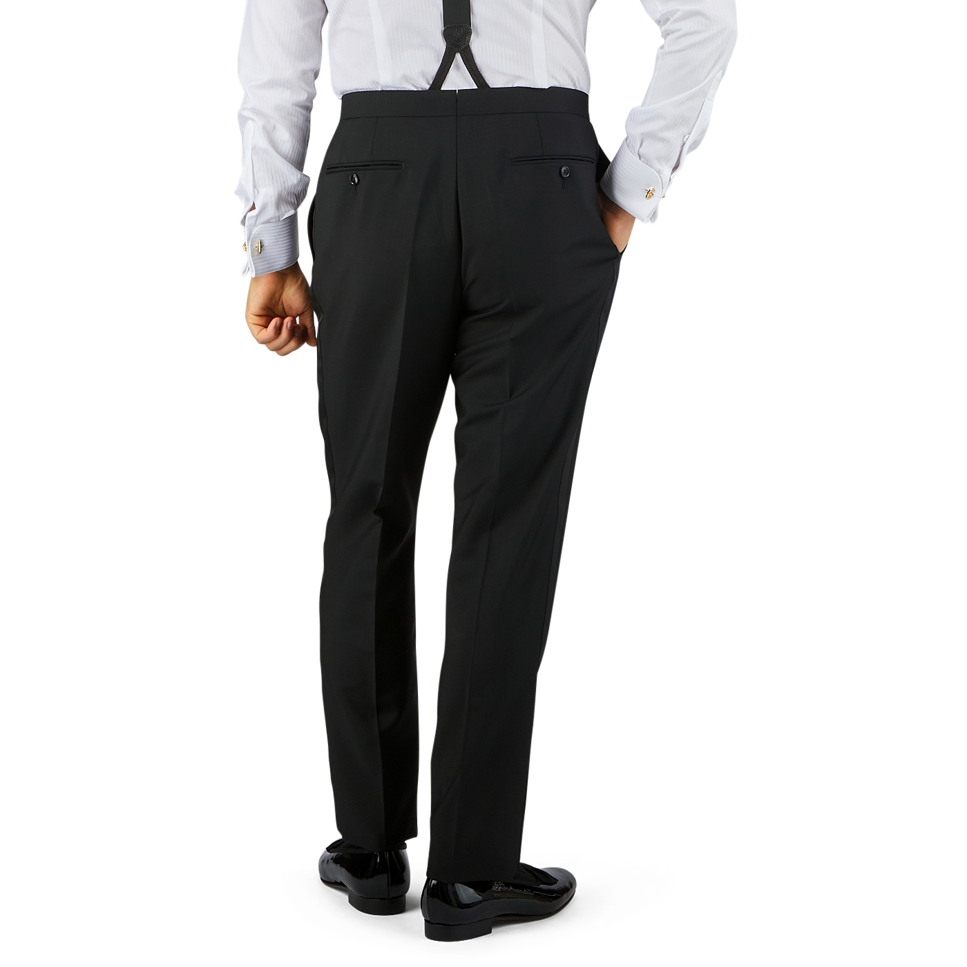 Man in Black Wool Mohair Tuxedo Pleated Trousers by Baltzar Sartorial held up by suspenders, wearing a white shirt with cufflinks, viewed from behind, standing against a plain background.