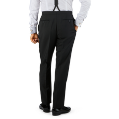 Man in Black Wool Mohair Tuxedo Pleated Trousers by Baltzar Sartorial held up by suspenders, wearing a white shirt with cufflinks, viewed from behind, standing against a plain background.