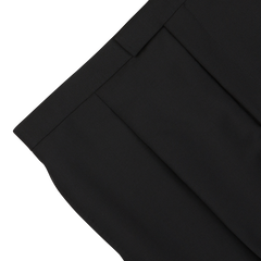 Close-up view of the waist and pleated front of a pair of Baltzar Sartorial Black Wool Mohair Tuxedo Pleated Trousers against a white background, showcasing their formal look.