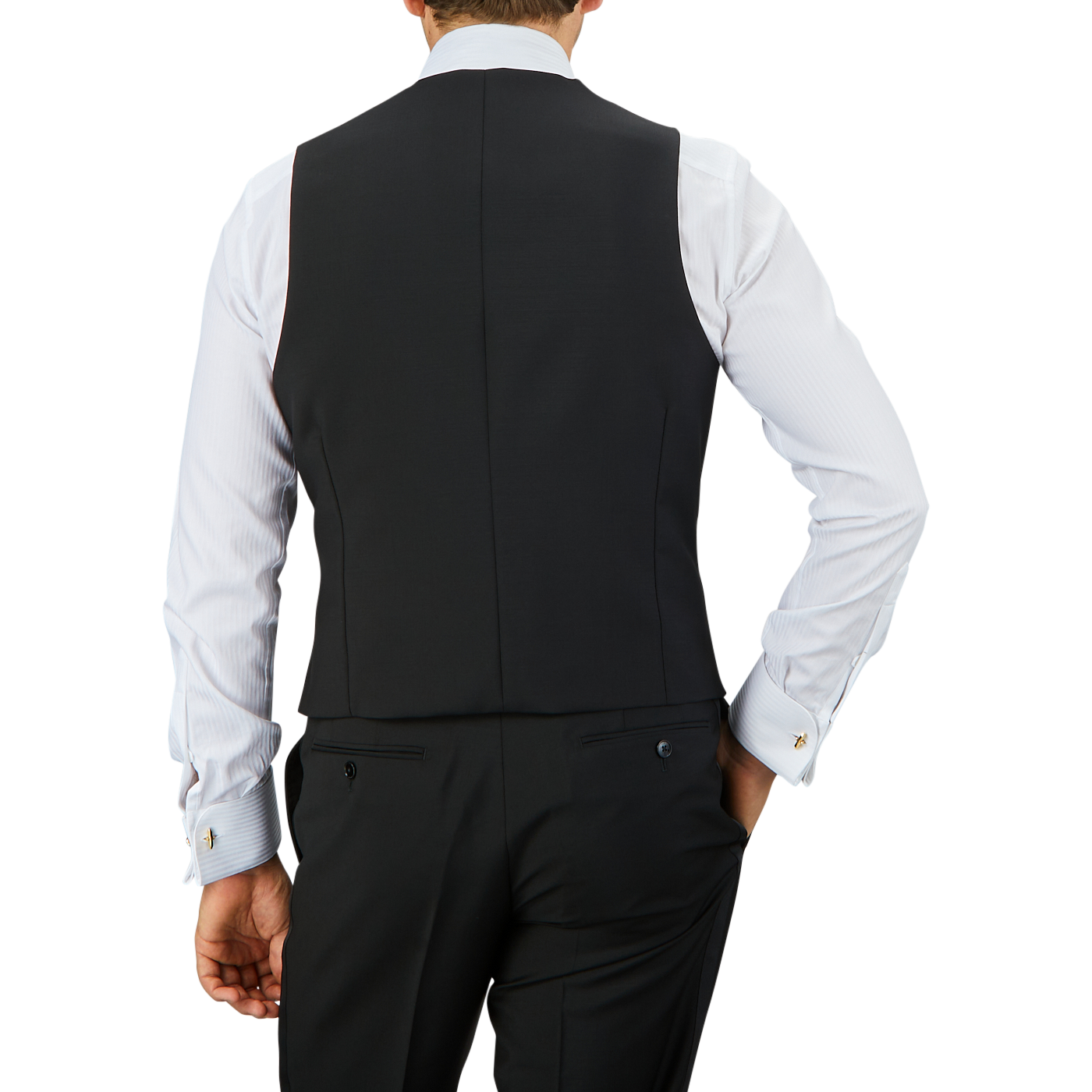 A person in a Baltzar Sartorial Black Wool Mohair Tuxedo Waistcoat and white dress shirt is seen from the back, with hands resting on hips.