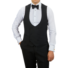 A person dressed in formal attire features a Black Wool Mohair Tuxedo Waistcoat by Baltzar Sartorial with a white dress shirt and black trousers, complemented by a stylish bow tie.