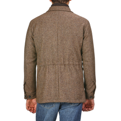 Back view of a person wearing a Brown Herringbone Wool Tweed Utility Jacket by Baltzar Sartorial and blue jeans, standing against a plain background.