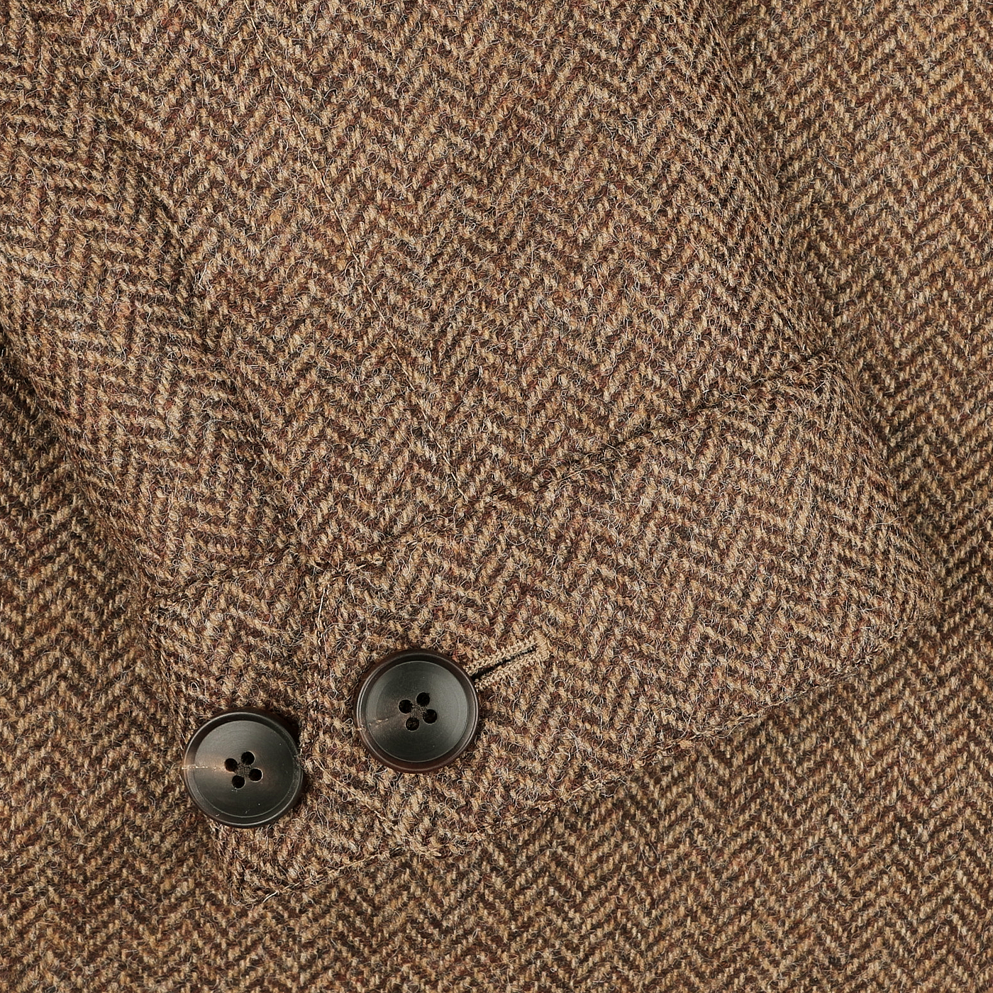 A close-up of a Brown Herringbone Wool Tweed Utility Jacket by Baltzar Sartorial highlights two black buttons on the sleeve.