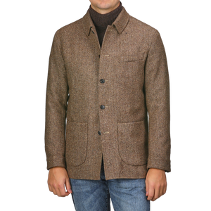 A person wearing a Brown Herringbone Wool Tweed Utility Jacket by Baltzar Sartorial over a dark sweater and blue jeans.