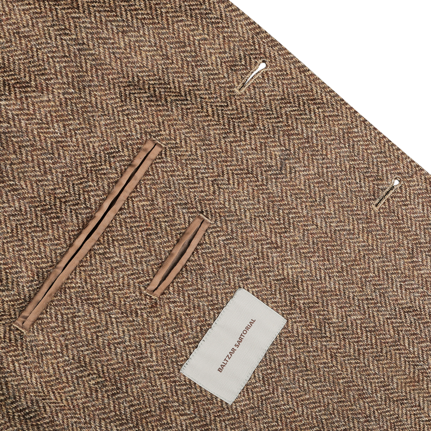 Close-up of a brown herringbone wool tweed utility jacket with two pockets and a label reading "Baltzar Sartorial" on the front, offering a sophisticated yet casual substitute for the classic utility jacket.