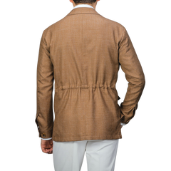 Rear view of someone in a Baltzar Sartorial Camel Brown Wool Silk Linen Safari Jacket, with a cinched waist and paired with white pants, making an ideal tailored blazer alternative.