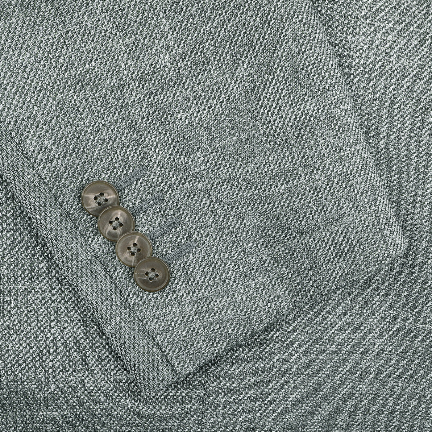 Close-up of the sleeve from Baltzar Sartorial's Green Wool Silk Linen Hopsack Blazer, featuring four brown buttons in a row.