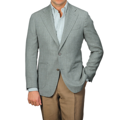 A man wearing a green wool silk linen hopsack blazer from Baltzar Sartorial over a striped shirt with brown pants, standing with one hand in his pocket.