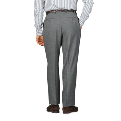 Dressed in a striped shirt and Baltzar Sartorial's Grey High-Twist Wool Pleated Trousers, a person stands with their back to the camera, exuding understated elegance.