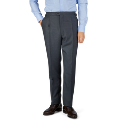 Man in a light blue shirt and Grey Super 100's Wool Pleated Suit Trousers by Baltzar Sartorial standing against a neutral background.