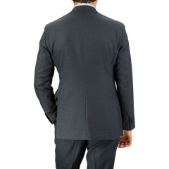 Rear view of a man wearing a tailored Baltzar Sartorial Grey Super 100's Wool Suit Jacket and pants, standing against a plain light grey background.