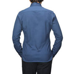 Someone is seen from the back against a plain background, wearing an Indigo Blue Cotton Piqué BD Popover Shirt by Baltzar Sartorial and black pants.