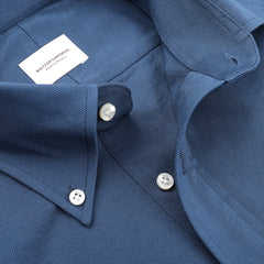 Close-up of Baltzar Sartorial's Indigo Blue Cotton Piqué BD Popover Shirt, showing its textured cotton fabric, a white label on the collar, and three visible white buttons.