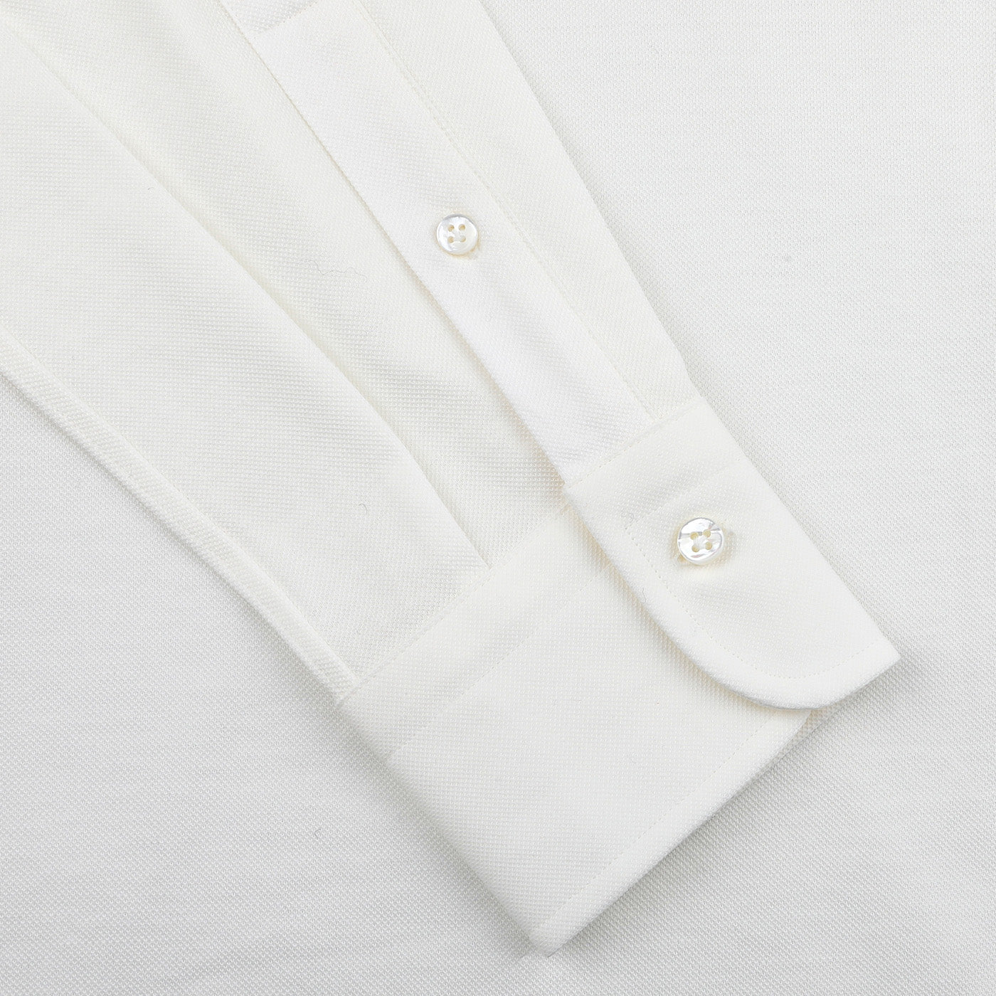 Close-up of an Ivory White Cotton Piqué BD Popover Shirt sleeve from Baltzar Sartorial, featuring a buttoned cuff with two visible white buttons. This piece enhances its sleek design, creating a classic aesthetic.