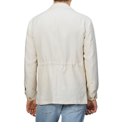 A person is seen from behind wearing a Baltzar Sartorial Light Beige Pure Linen Safari Jacket with blue jeans, exuding effortless style against a neutral backdrop.