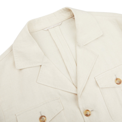 A close-up of the Light Beige Pure Linen Safari Jacket by Baltzar Sartorial, crafted from mid-weight linen with two front pockets and wooden buttons, laid flat on a white surface.