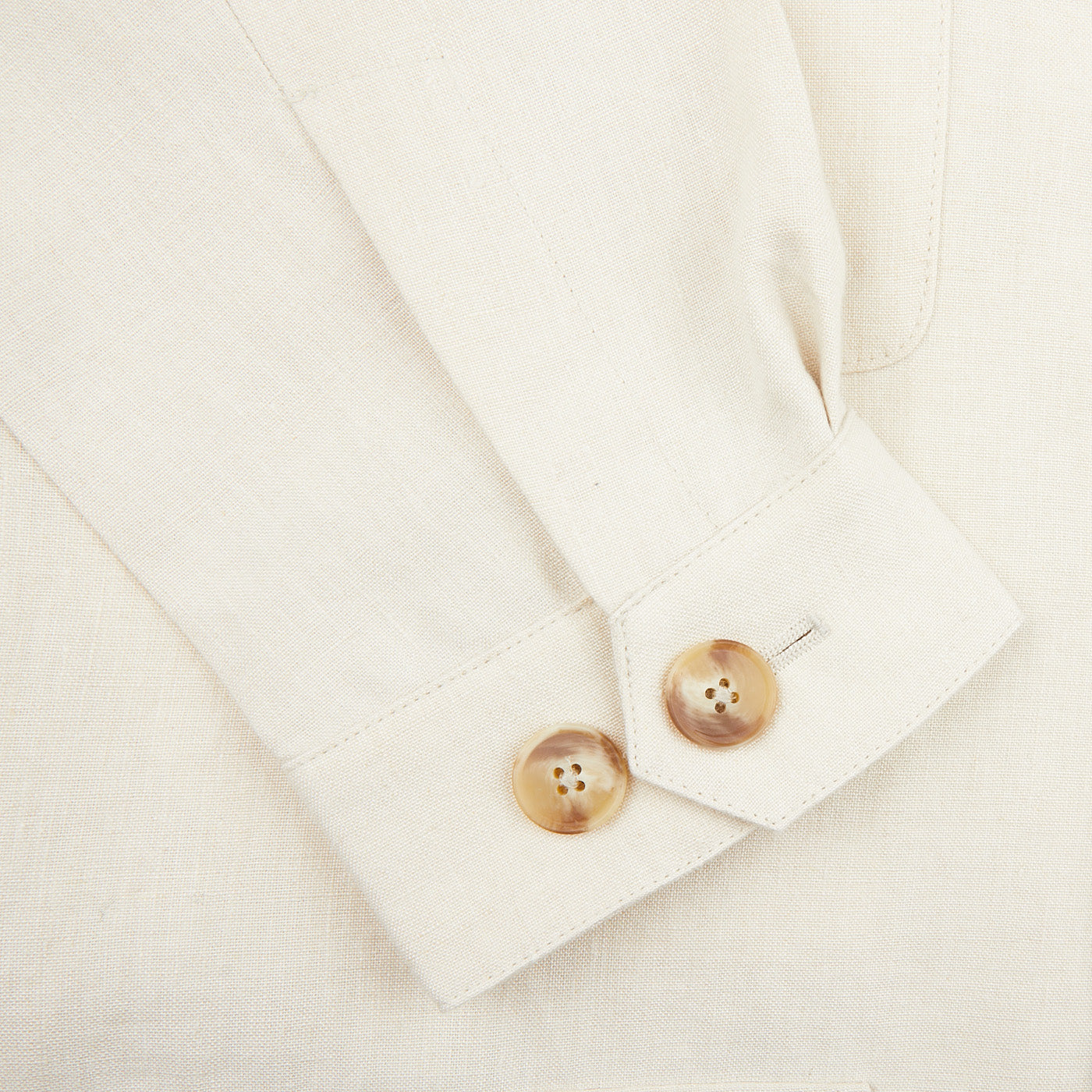 Close-up of the Light Beige Pure Linen Safari Jacket sleeve by Baltzar Sartorial, featuring two light brown cuff buttons, crafted from mid-weight linen and displayed on a flat surface.