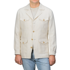 A man in a Light Beige Pure Linen Safari Jacket by Baltzar Sartorial, featuring multiple pockets and mid-weight linen, stands beside light blue jeans against a plain backdrop.