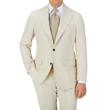 A man is posing in a Light Beige Pure Linen Suit Jacket by Baltzar Sartorial, consisting of a suit jacket and tailored trousers.