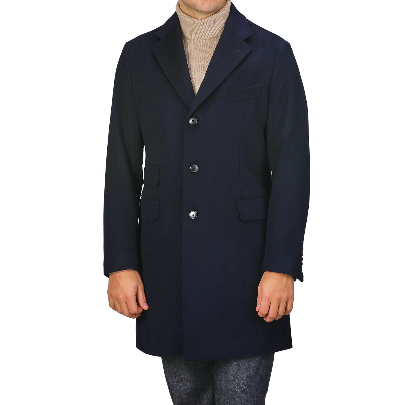 A person is dressed in a Baltzar Sartorial Navy Blue Loro Piana Wool Tailored Coat, showcasing a single-breasted design with three buttons and flap pockets. Underneath, they wear a beige turtleneck sweater paired with gray pants, making it an ideal outfit for any weather due to the innovative Rain System.