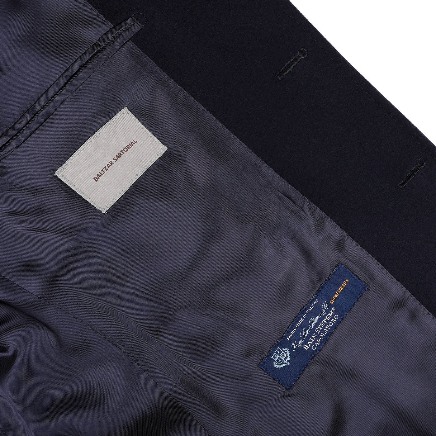 Inside view of the Navy Blue Loro Piana Wool Tailored Coat by Baltzar Sartorial, featuring two labels: one from "Savile Row" and another from "Scabal Savile Row, Fine English Clothiers." The lining is dark blue, highlighting the exquisite craftsmanship.