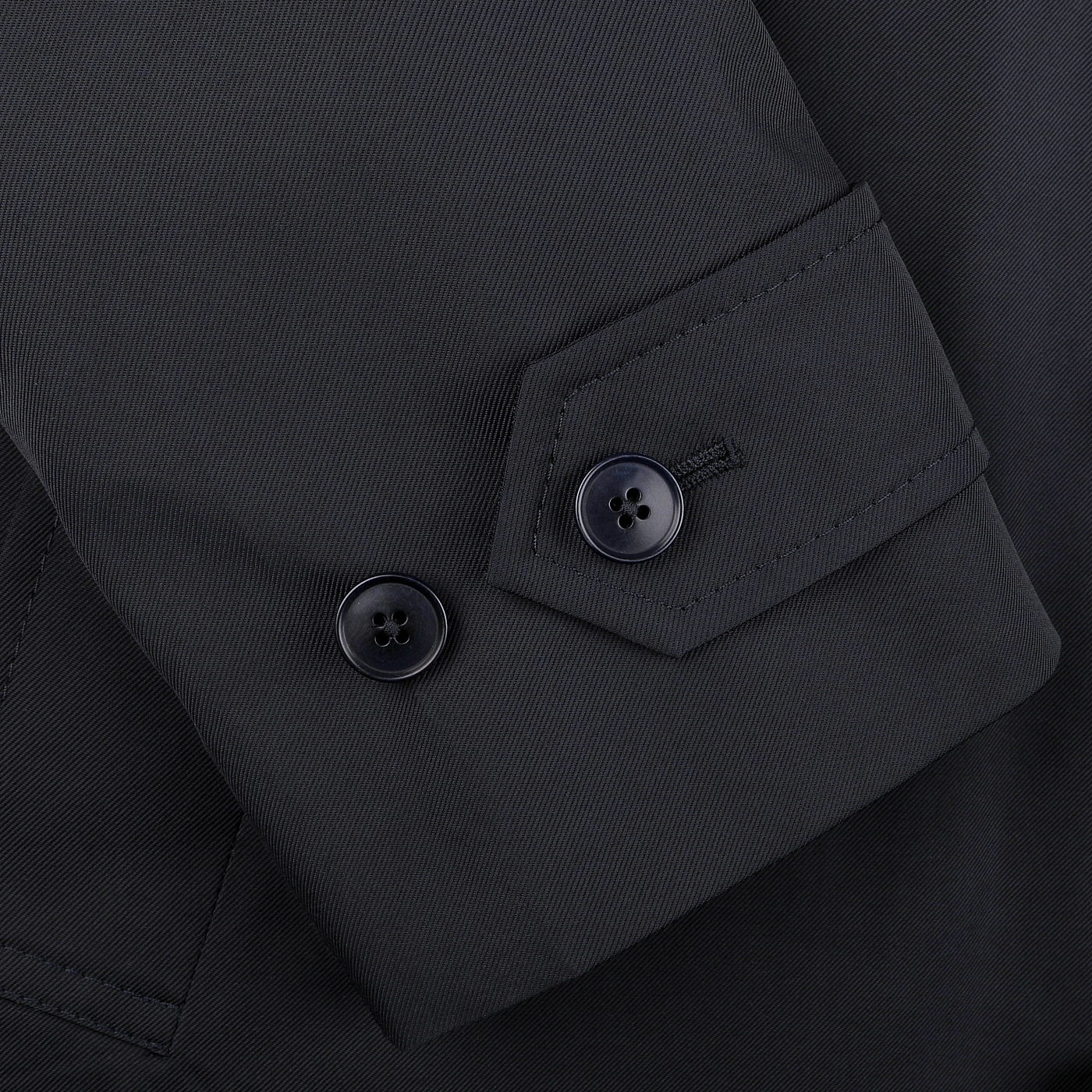 Close-up of a navy blue car coat sleeve by Baltzar Sartorial, featuring two sleek black buttons on the cuff, complemented by a durable nylon outer for weather resistance.