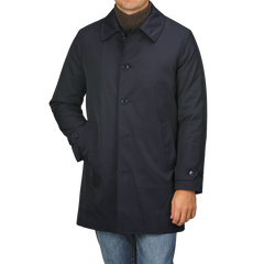 A person is standing against a plain background wearing the Navy Blue Nylon Thermore Padded Car Coat by Baltzar Sartorial, featuring button closure and Thermore Ecodown lining, paired with jeans.