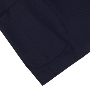 Close-up of a Navy Blue Wool Hopsack Blazer fabric with a stitched hem on a white background by Baltzar Sartorial.