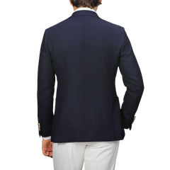 A person showcases timeless elegance from the back in a Baltzar Sartorial Navy Blue Wool Mock Leno DB Club Blazer with white pants against a plain background.