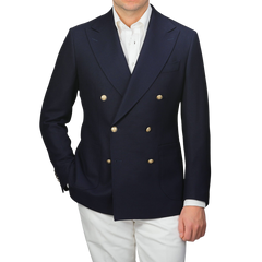 Wearing a Navy Blue Wool Mock Leno DB Club Blazer by Baltzar Sartorial with gold buttons, paired with a white shirt and white pants, exudes refined elegance.