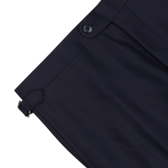 Close-up of a Baltzar Sartorial Navy Super 100's Wool Flat Front Suit Trousers waistband with a button closure and a metal clasp detail on a white background.