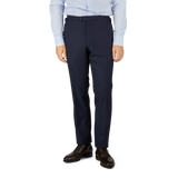 A cropped image of a man dressed in a light blue shirt and Baltzar Sartorial Navy Super 100's Wool Flat Front Suit Trousers with black dress shoes, standing against a white background.