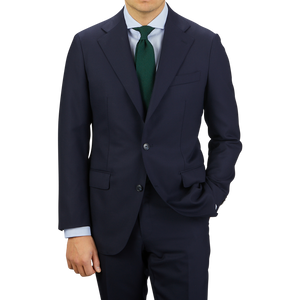 Man in a Baltzar Sartorial Navy Super 100's Wool Suit Jacket with a teal tie standing against a grey background.