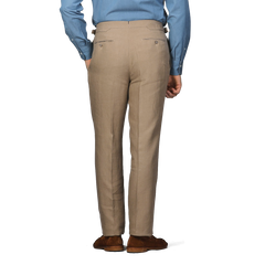 A man in a blue shirt and Taupe Beige Pure Linen Pleated Trousers from Baltzar Sartorial stands with his hands at his sides, viewed from behind.