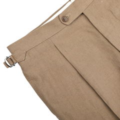 The Taupe Beige Pure Linen Pleated Trousers by Baltzar Sartorial feature a tailored fit with pleat details and a button and buckle closure.