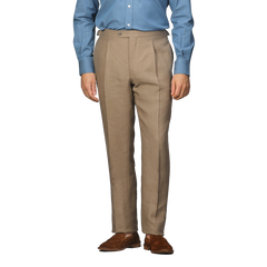 The image shows a person wearing a blue dress shirt, Taupe Beige Pure Linen Pleated Trousers by Baltzar Sartorial, and brown dress shoes, focused on the attire from neck to feet.