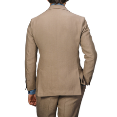 Back view of a person wearing a taupe beige pure linen suit jacket and blue shirt, hands in pockets, against a plain background. This Baltzar Sartorial outfit is completed with impeccably tailored trousers.