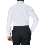 The back view of a man in a Baltzar Sartorial White Striped Cotton Dinner Handmade Shirt with mother-of-pearl buttons and black slacks.