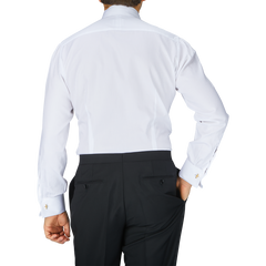 The back view of a man in a Baltzar Sartorial White Striped Cotton Dinner Handmade Shirt with mother-of-pearl buttons and black slacks.