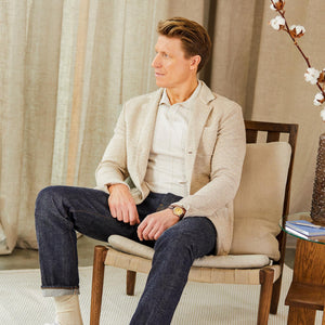 Maurizio Baldassari, wearing a Maurizio Baldassari Beige Melange Cotton Mouline Knitted Jacket, is sitting in a chair.