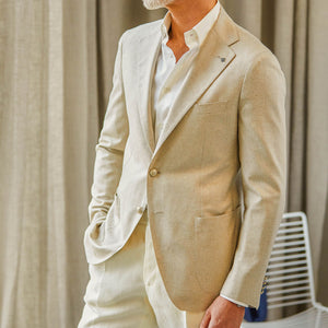 A person wearing a Beige Melange Silk Twill Vesuvio Tagliatore blazer paired with a white shirt, standing with one hand in their pocket.