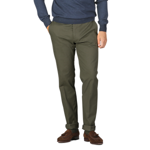 A male model is standing in Berwich Army Green Cotton Twill Flat Front Trousers and brown suede shoes, with his hands in his pockets. He is wearing a navy-blue long-sleeve top against a plain white background.