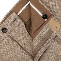 A close-up of Berwich's Beige Herringbone Wool Tweed Trousers highlights the taupe beige fabric and herringbone pattern, complete with a button and zip closure, showcasing the pure wool interior waistband and pockets.