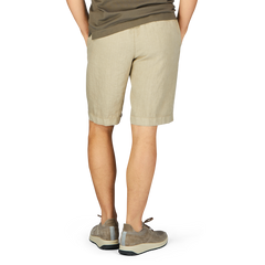 Person standing with their back to the camera, wearing contemporary fit Berwich Beige Washed Linen Drawstring Shorts and gray sneakers.