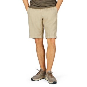 Person wearing contemporary fit, Berwich beige washed linen drawstring shorts and casual sneakers standing against a plain background.