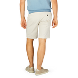 Person standing in Berwich cream beige cotton blend Bermuda shorts and casual shoes with their back to the camera.